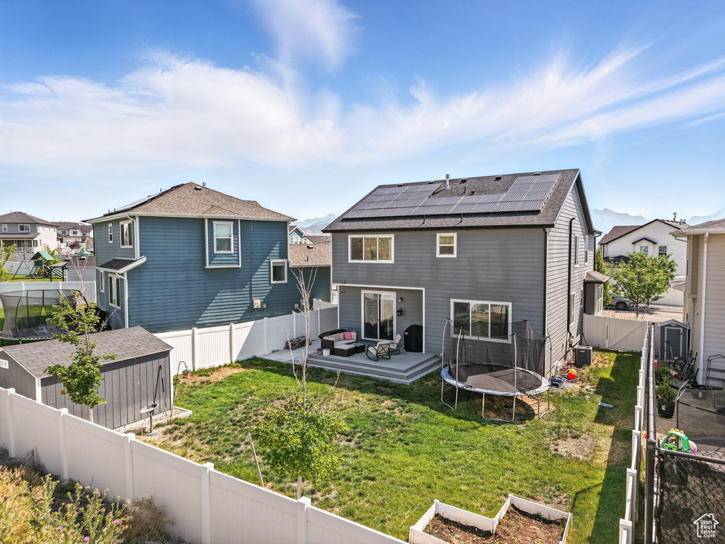 Back of house with solar panels, a fenced backyard, a residential view, and a shed