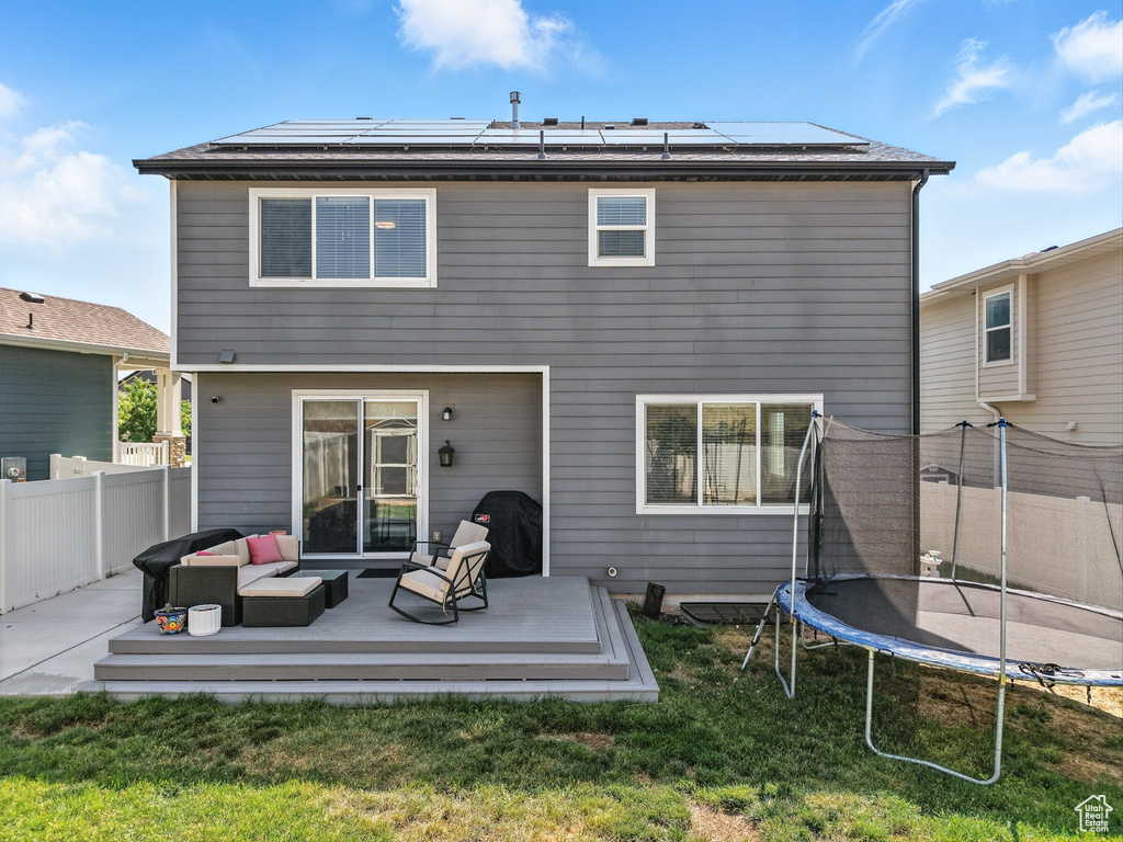 Back of property with a trampoline, an outdoor hangout area, a wooden deck, and solar panels