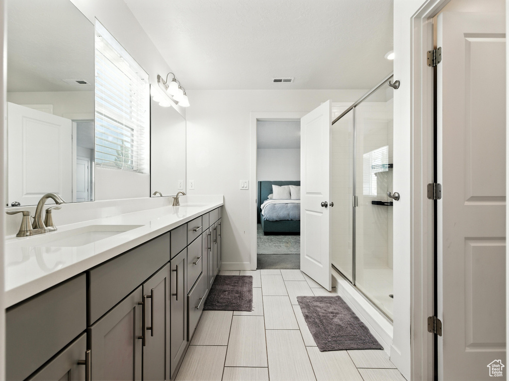 Ensuite bathroom with double vanity, a shower stall, and tile patterned floors