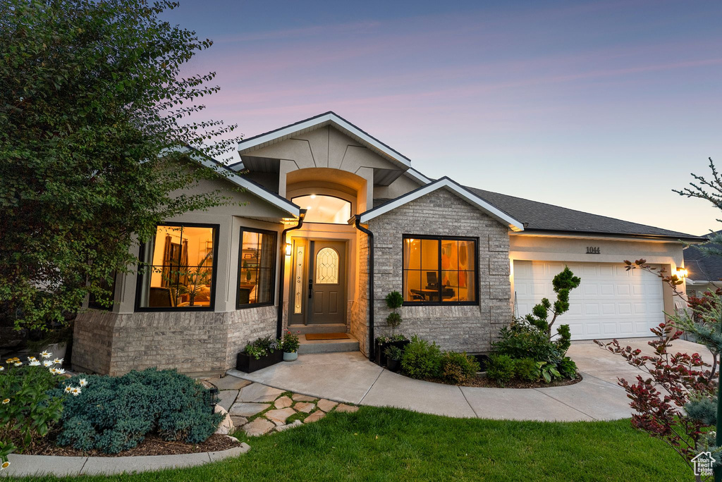 View of front of property featuring an attached garage, concrete driveway, stone siding, and stucco siding