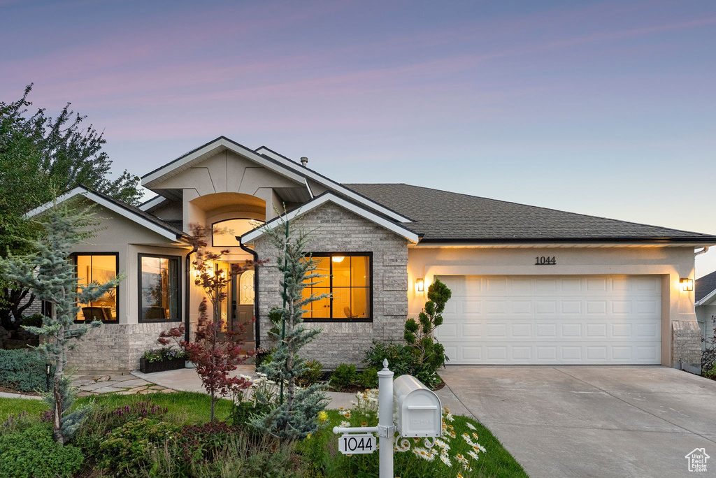 View of front of house with driveway, a garage, stone siding, and stucco siding