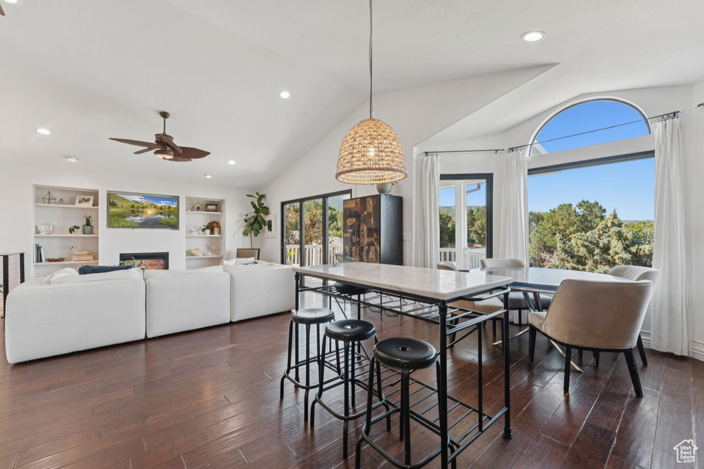 Dining area with ceiling fan, lofted ceiling, dark wood-style flooring, a glass covered fireplace, and recessed lighting