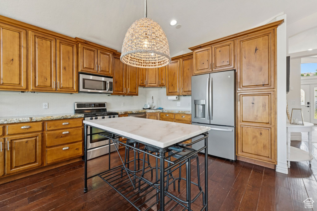 Kitchen with stainless steel appliances, brown cabinetry, dark wood-style flooring, decorative light fixtures, and lofted ceiling
