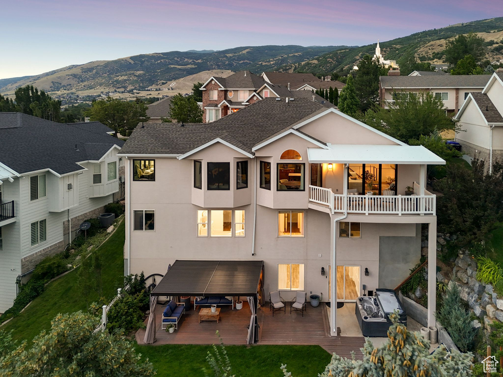 Back of house at dusk featuring a balcony, stucco siding, a mountain view, and an outdoor hangout area