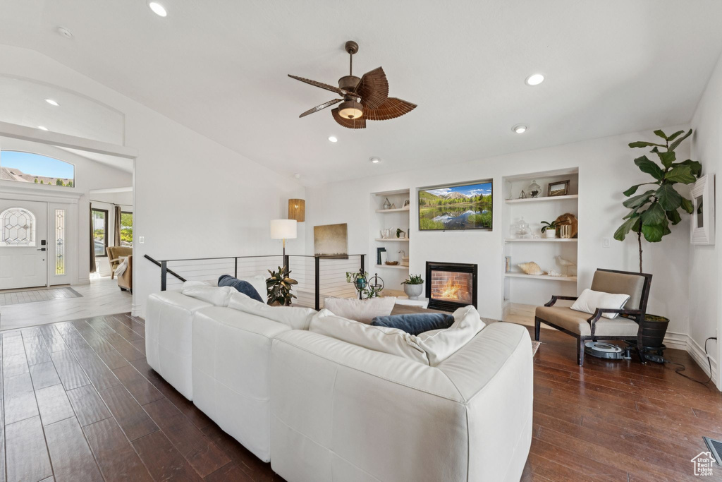 Living area with ceiling fan, a glass covered fireplace, dark wood-type flooring, recessed lighting, and built in shelves