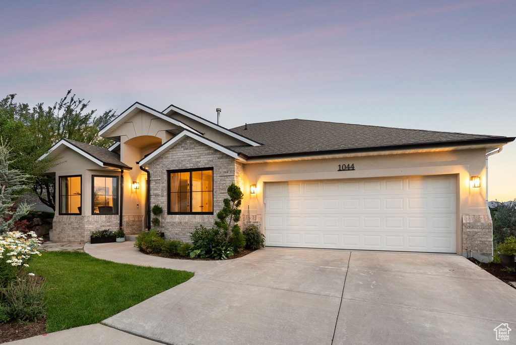 View of front of home featuring driveway, an attached garage, stone siding, a shingled roof, and a front lawn