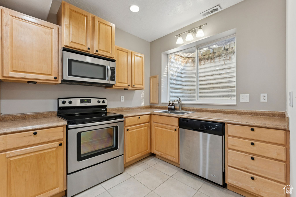 Kitchen featuring appliances with stainless steel finishes, light brown cabinets, light tile patterned floors, and light countertops