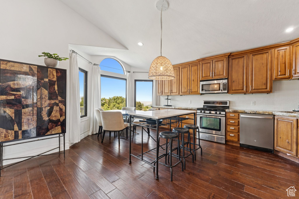 Kitchen featuring appliances with stainless steel finishes, brown cabinetry, vaulted ceiling, dark wood-style floors, and recessed lighting