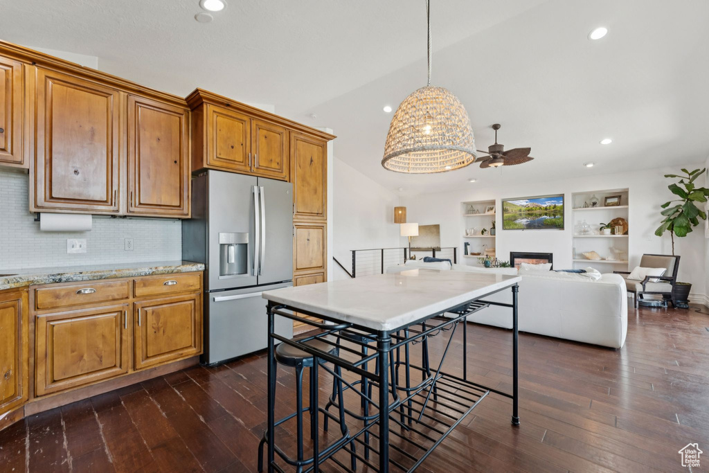 Kitchen featuring stainless steel fridge, ceiling fan, brown cabinets, a fireplace, and dark wood-style floors
