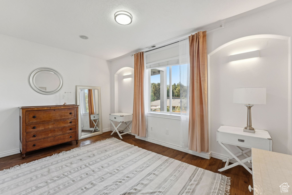 Bedroom featuring arched walkways and dark wood-style floors