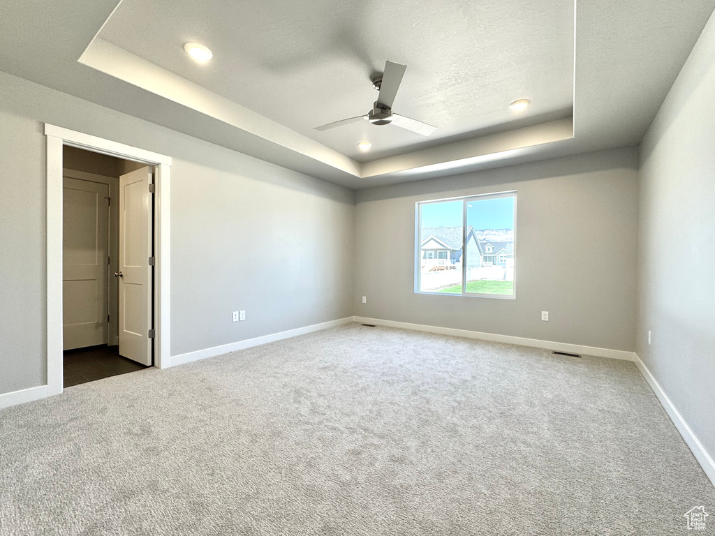 Carpeted spare room with a raised ceiling, ceiling fan, and recessed lighting