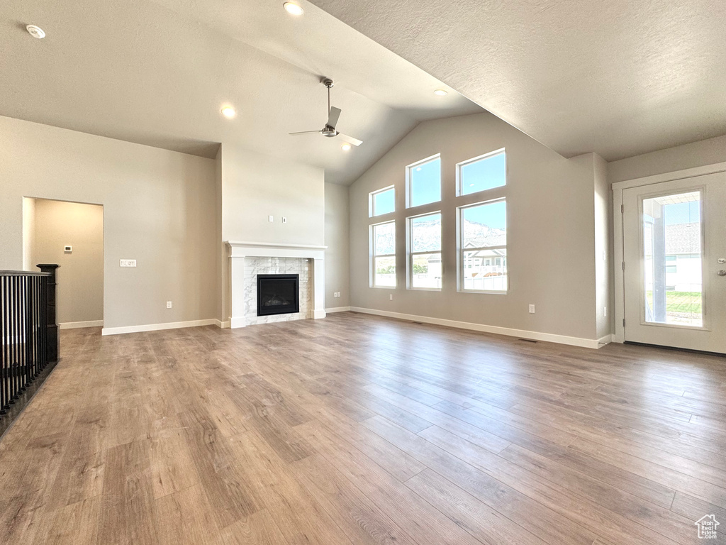 Unfurnished living room featuring a ceiling fan, wood finished floors, a fireplace, high vaulted ceiling, and a textured ceiling