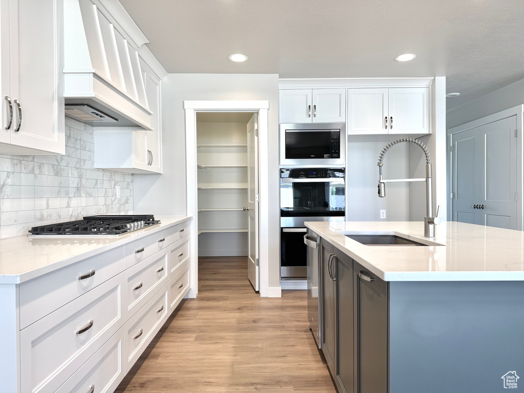 Kitchen with stainless steel appliances, premium range hood, light wood-style floors, white cabinets, and recessed lighting
