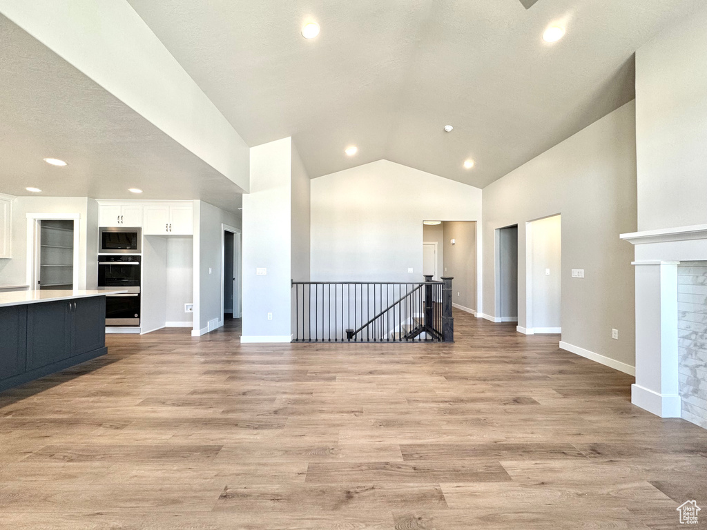 Unfurnished living room featuring lofted ceiling, recessed lighting, light wood finished floors, and a glass covered fireplace