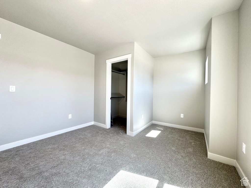 Unfurnished bedroom featuring dark colored carpet, a spacious closet, and a closet