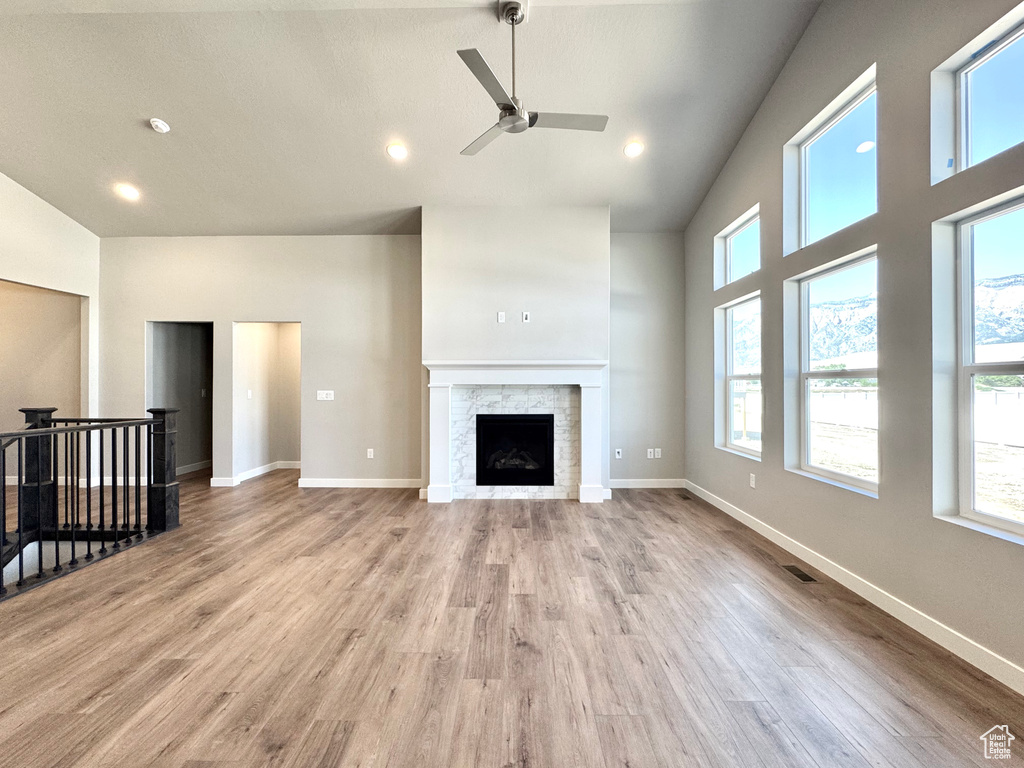 Unfurnished living room featuring ceiling fan, plenty of natural light, high vaulted ceiling, wood finished floors, and a stone fireplace