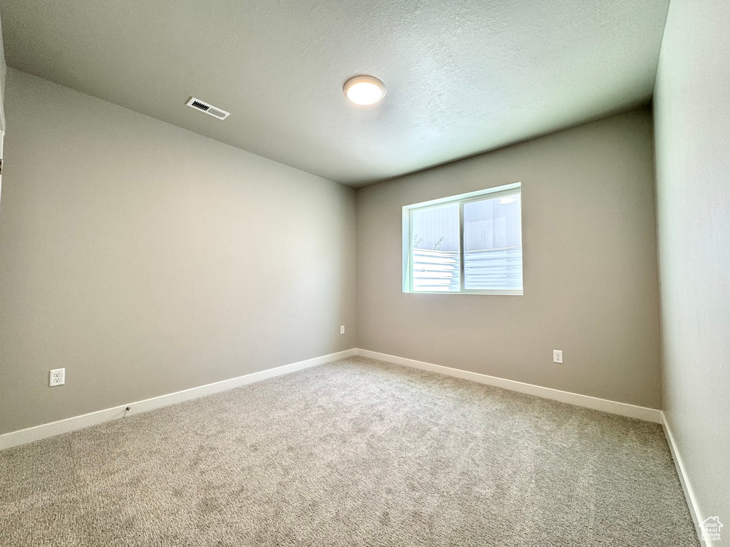 Empty room with light colored carpet and a textured ceiling