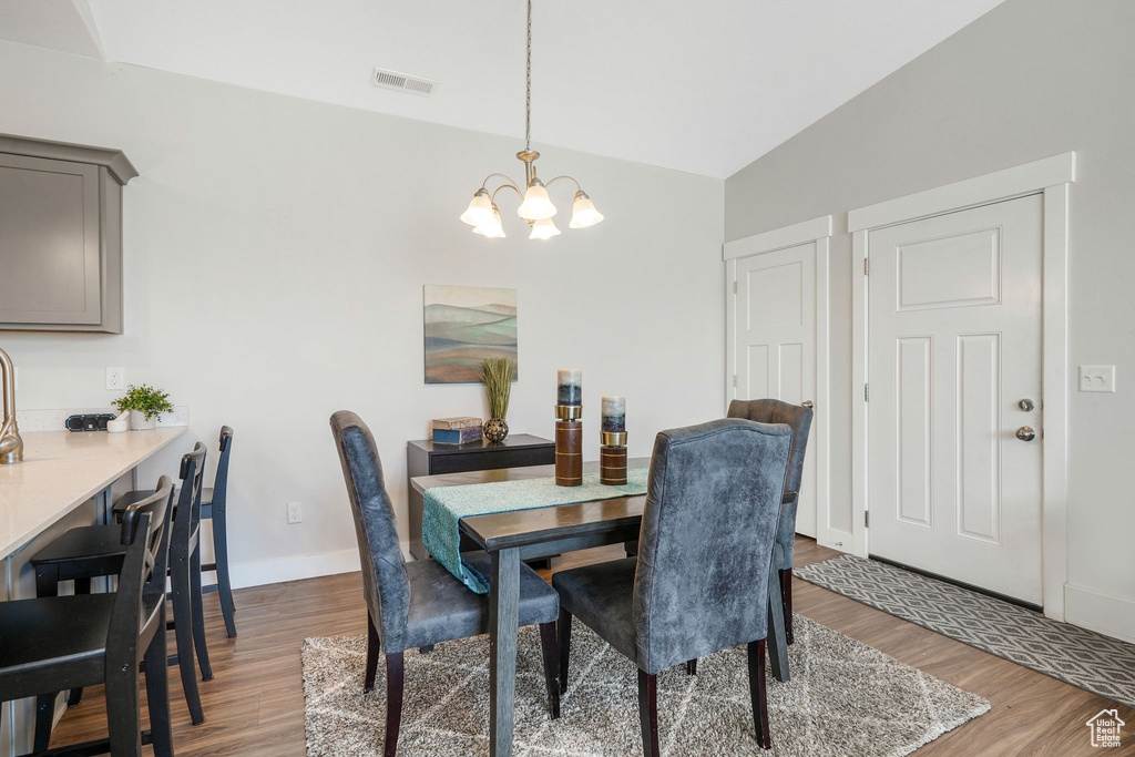 Dining space with a chandelier, wood finished floors, and vaulted ceiling