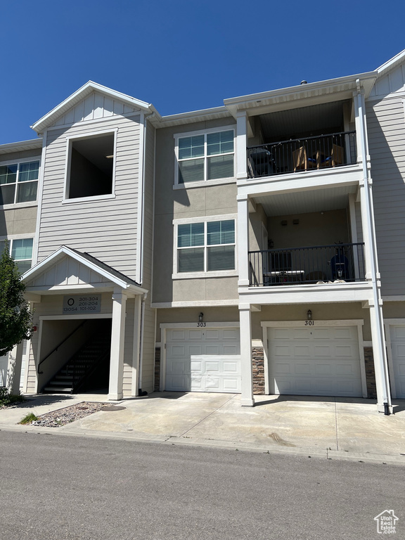 Multi unit property featuring a garage, driveway, board and batten siding, a balcony, and stucco siding