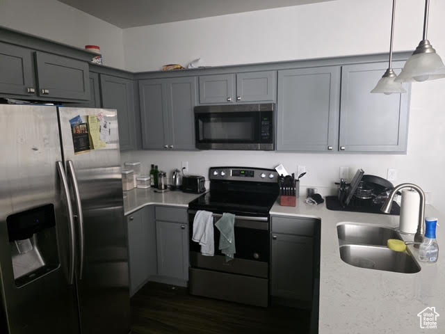 Kitchen featuring stainless steel appliances, gray cabinetry, hanging light fixtures, dark wood-style flooring, and light stone countertops