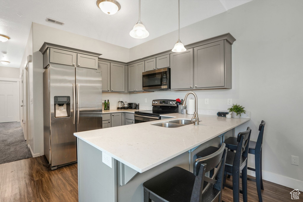 Kitchen with gray cabinetry, stainless steel appliances, a peninsula, dark wood finished floors, and a breakfast bar