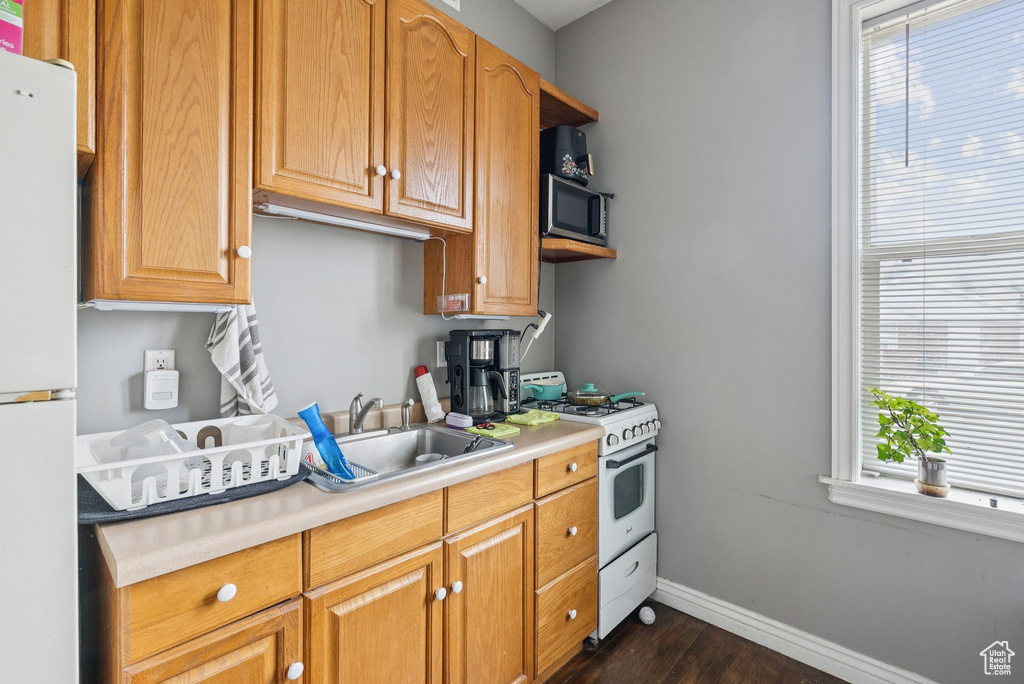 Kitchen with white appliances, dark wood-style flooring, light countertops, and healthy amount of natural light
