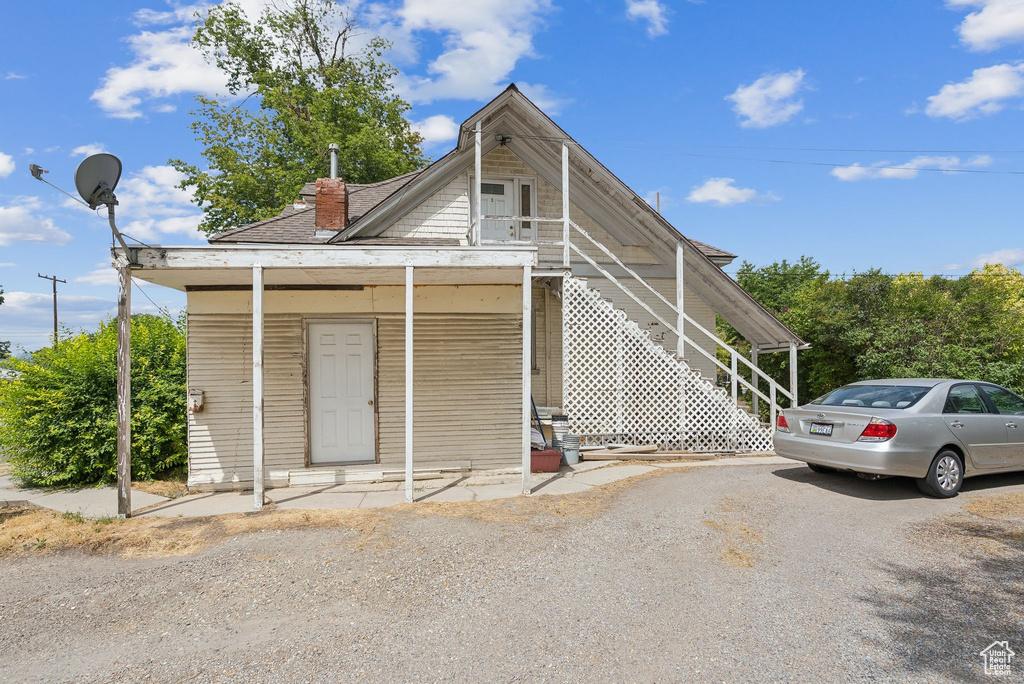 View of front facade featuring a chimney, asphalt driveway, roof with shingles, and stairway