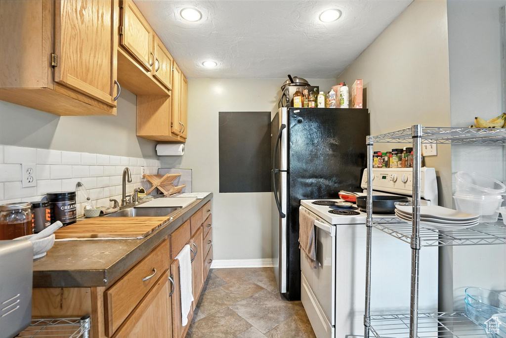 Kitchen with white range with electric cooktop, decorative backsplash, recessed lighting, light stone finish flooring, and dark countertops