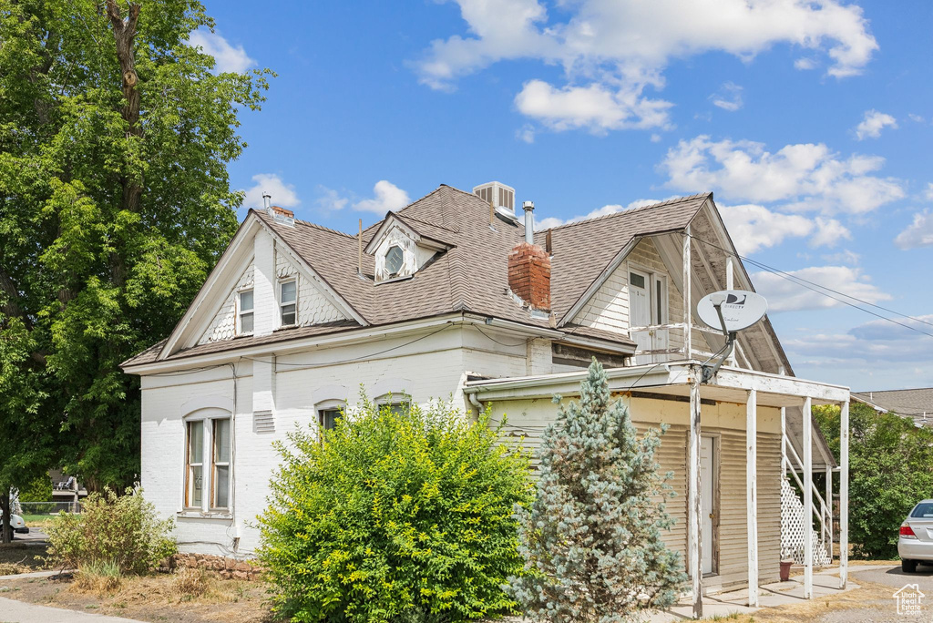 View of side of home featuring a shingled roof, stairway, a chimney, and brick siding