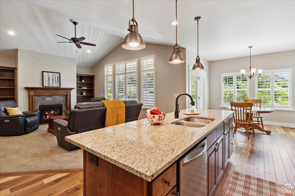 Kitchen featuring stainless steel dishwasher, healthy amount of natural light, light wood finished floors, a warm lit fireplace, and lofted ceiling