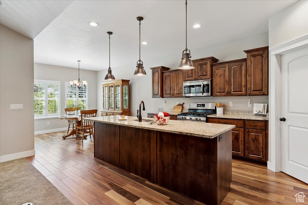 Kitchen featuring appliances with stainless steel finishes, wood finished floors, recessed lighting, light stone countertops, and a kitchen island with sink