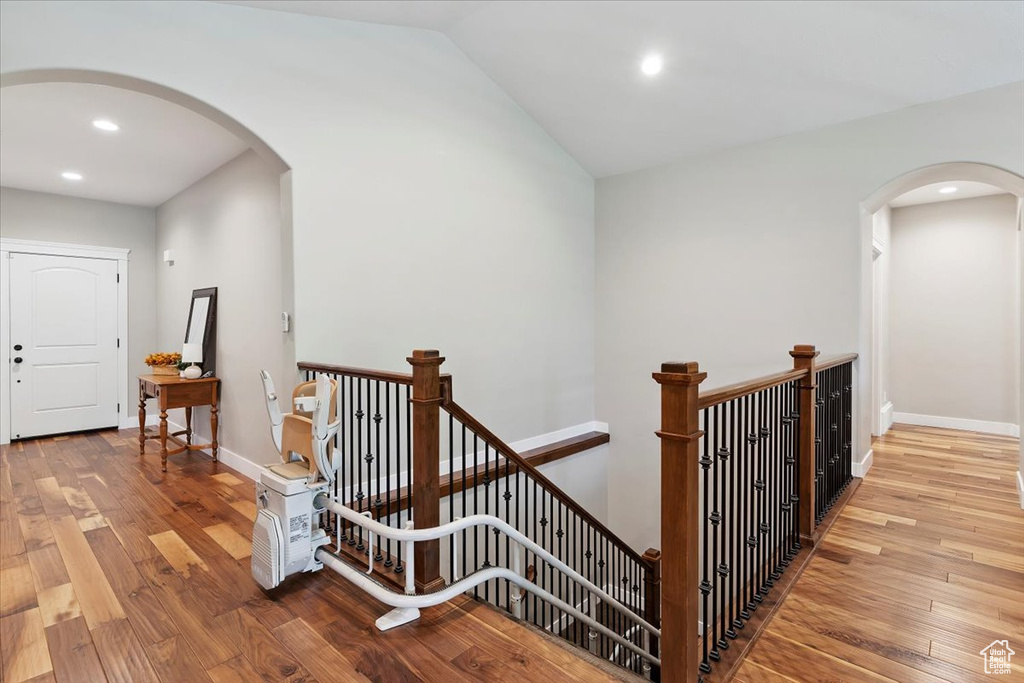 Hallway with an upstairs landing, arched walkways, wood finished floors, recessed lighting, and lofted ceiling
