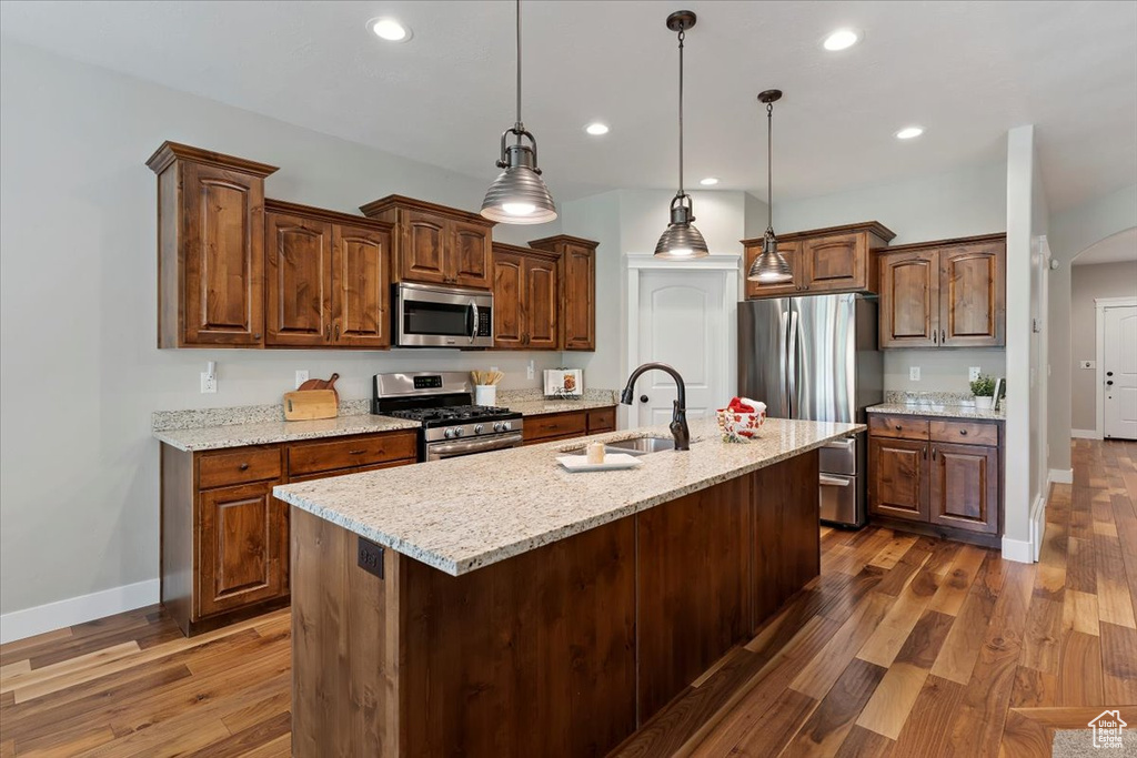 Kitchen with stainless steel appliances, arched walkways, dark wood finished floors, recessed lighting, and a center island with sink