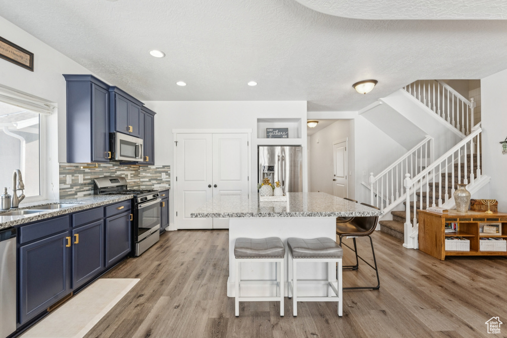 Kitchen featuring stainless steel appliances, blue cabinets, light wood-style floors, a kitchen bar, and recessed lighting