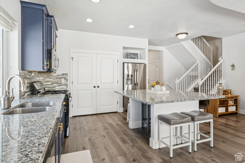 Kitchen featuring blue cabinetry, stainless steel appliances, a kitchen bar, wood finished floors, and recessed lighting