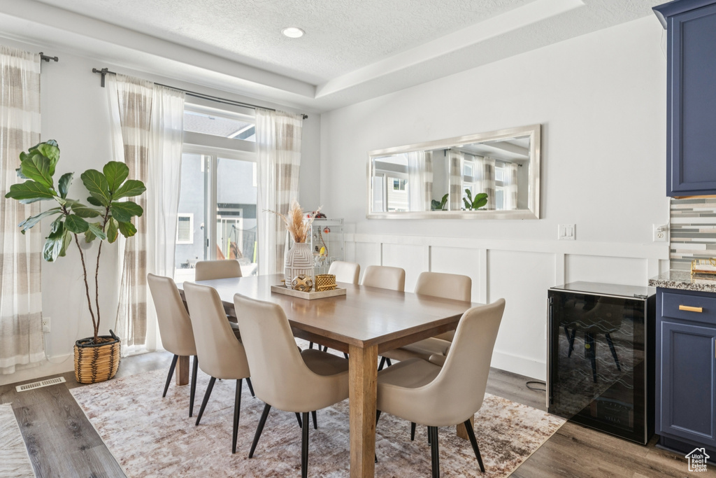 Dining room featuring beverage cooler, wood finished floors, bar area, and a textured ceiling