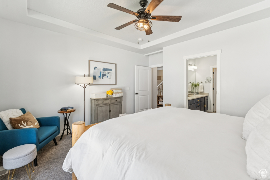 Carpeted bedroom featuring a raised ceiling, ensuite bathroom, and ceiling fan