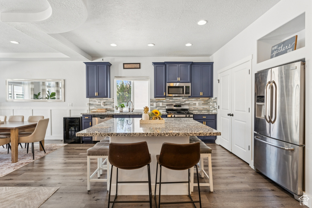 Kitchen featuring stainless steel appliances, blue cabinetry, a breakfast bar area, backsplash, and a textured ceiling