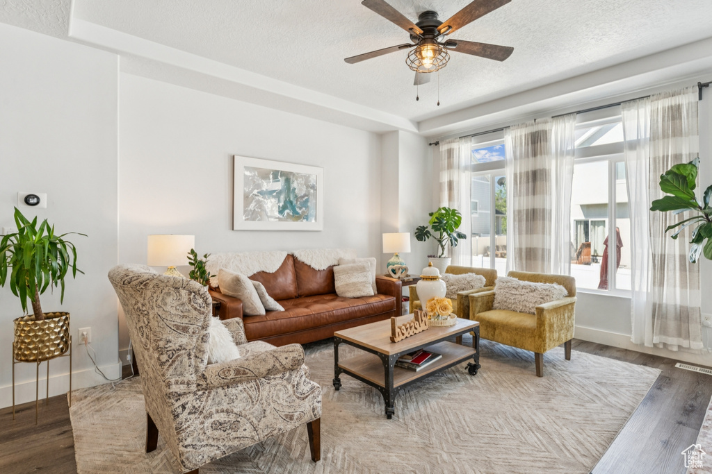 Living area featuring wood finished floors, ceiling fan, a raised ceiling, and a textured ceiling