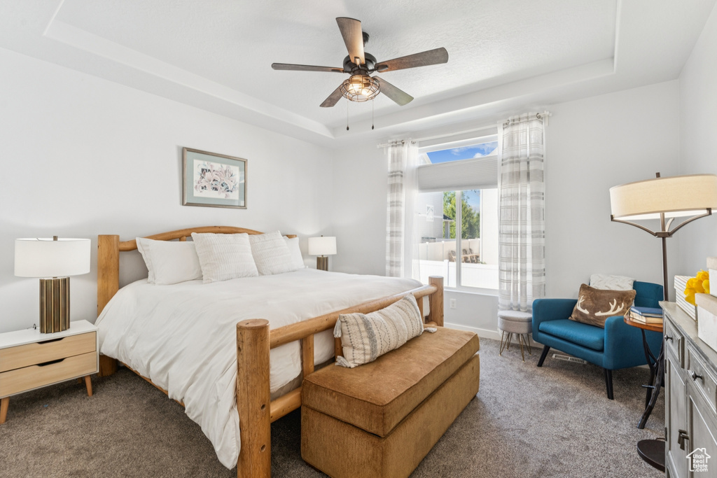 Carpeted bedroom featuring a raised ceiling and ceiling fan