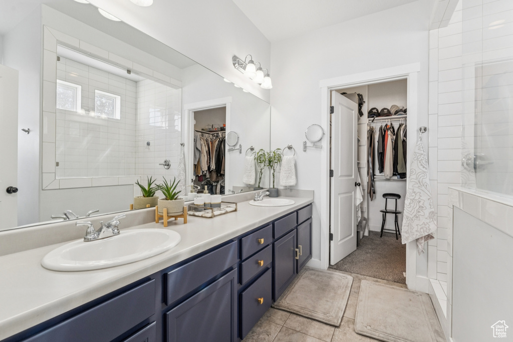 Bathroom with a spacious closet, double vanity, tile patterned flooring, and tiled shower