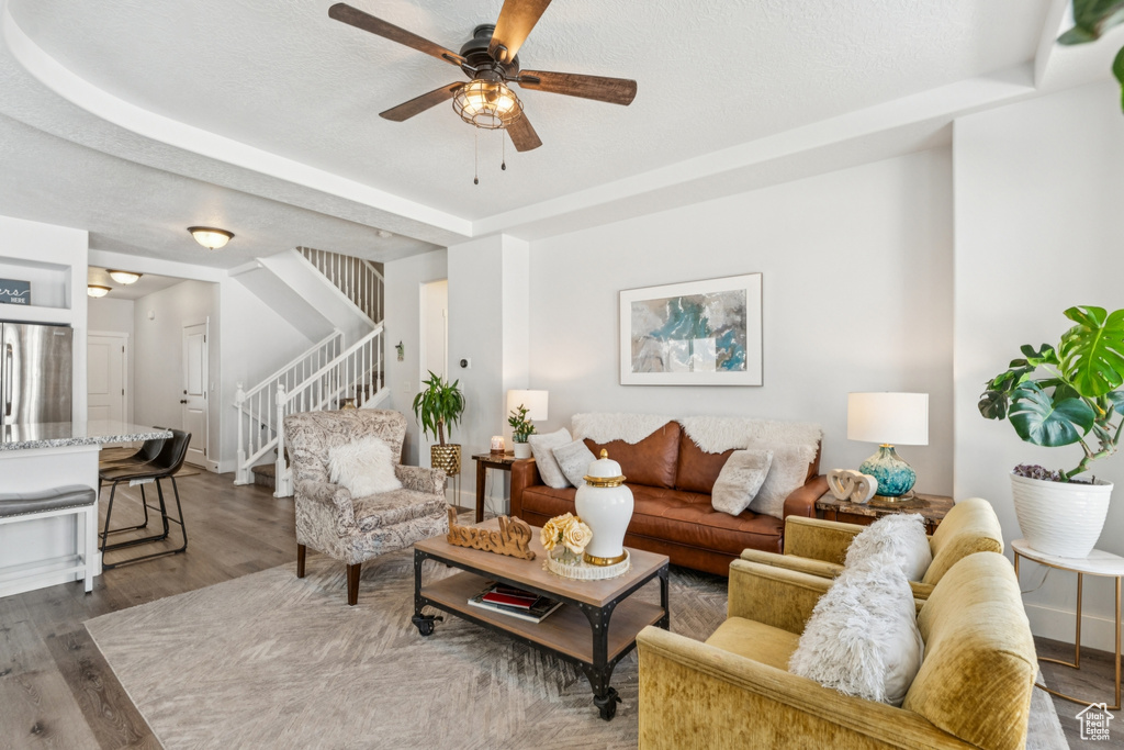 Living room featuring stairway, ceiling fan, wood finished floors, and a raised ceiling