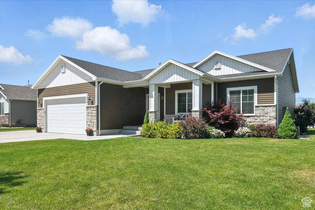 Craftsman house featuring stone siding, driveway, a porch, a front yard, and a garage
