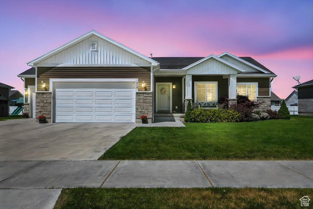 View of front of house featuring stone siding, concrete driveway, and a lawn
