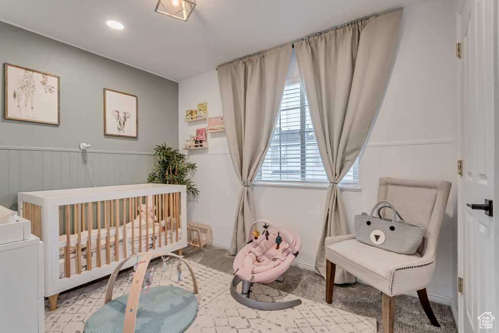 Carpeted bedroom featuring a crib and a wainscoted wall
