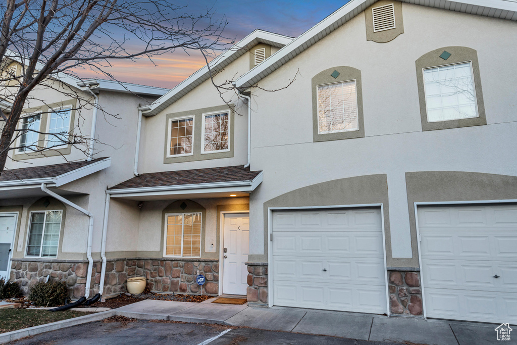 View of property with stone siding, stucco siding, an attached garage, and driveway