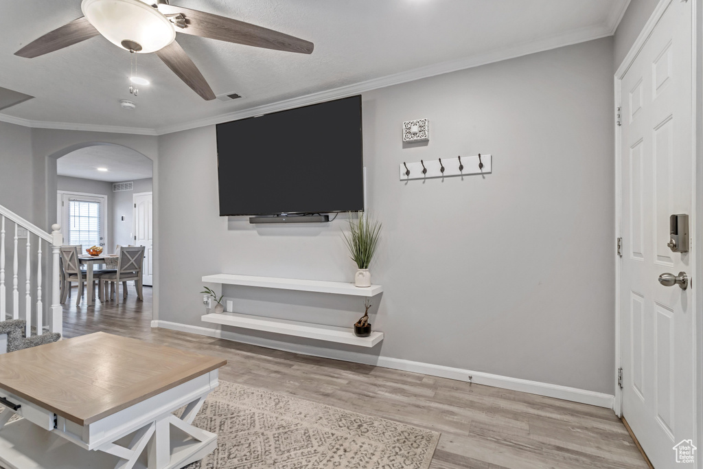 Living area featuring arched walkways, wood finished floors, stairs, ceiling fan, and crown molding