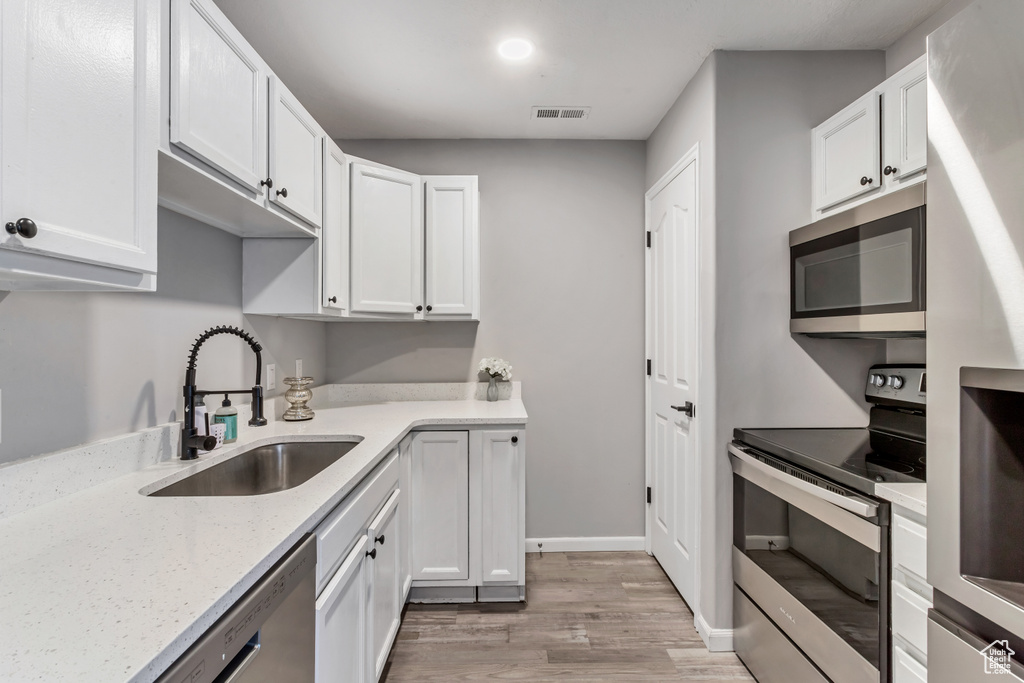 Kitchen featuring appliances with stainless steel finishes, light wood finished floors, white cabinetry, and light stone countertops