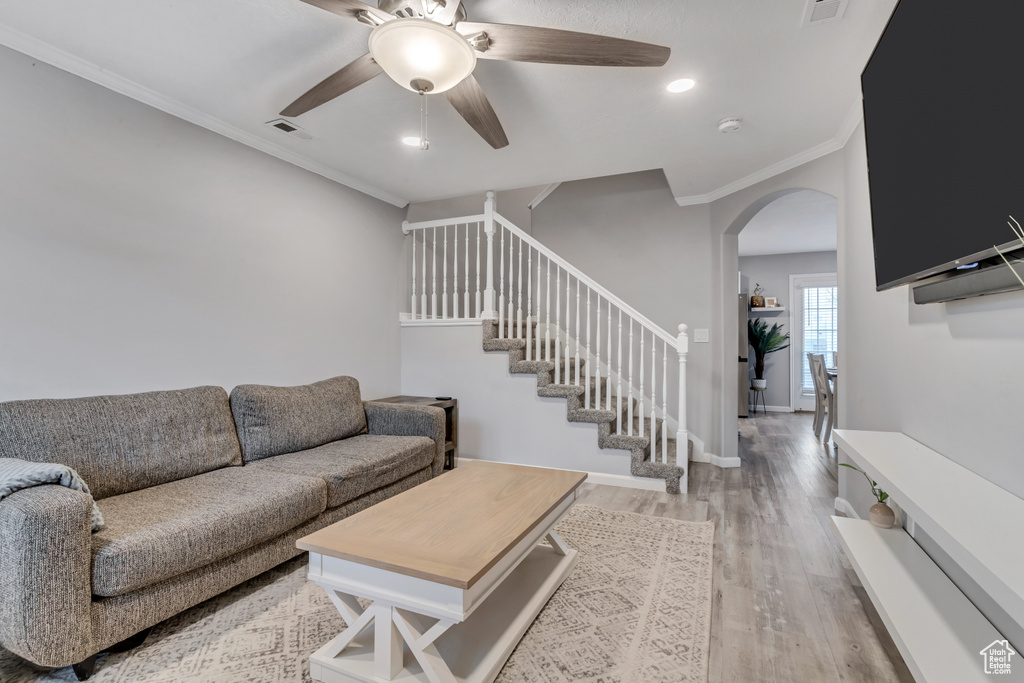 Living area featuring arched walkways, a ceiling fan, ornamental molding, light wood-type flooring, and stairs