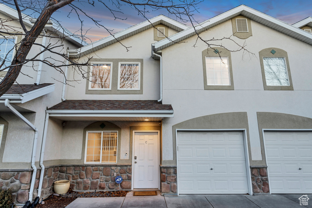 View of property with stucco siding, stone siding, a garage, and concrete driveway